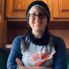 A white woman in glasses poses next to some cabinets.
