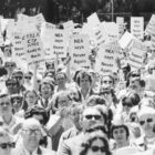 Black and white photograph of people with signs saying “NEA says Never again”.
