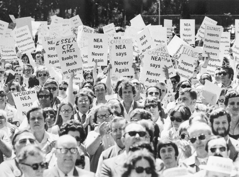 Black and white photograph of people with signs saying “NEA says Never again”.