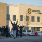 People gather, several with arms and fists raised, outside an Amazon fulfillment center.