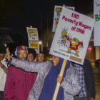 People march at night with signs saying "We Keep Campus Beautiful, Teamsters Local 320" and "END Poverty Wages at UMN.".