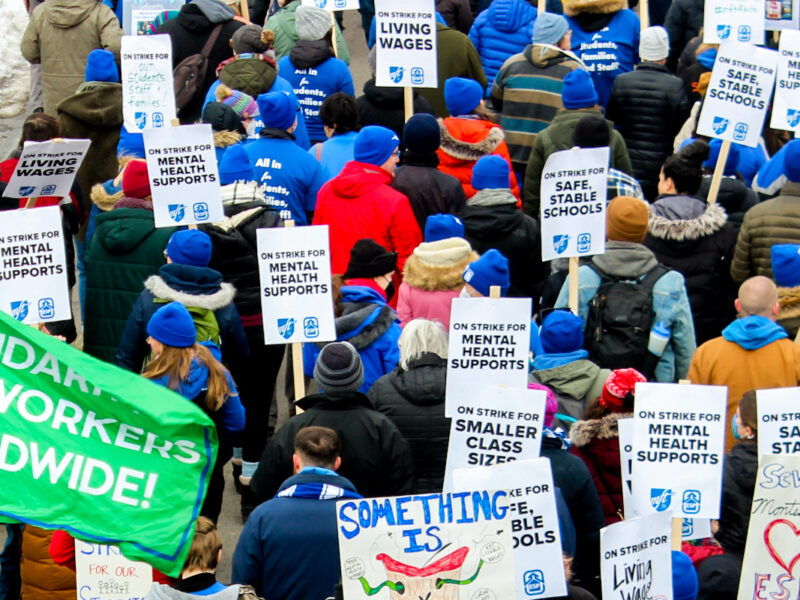 People march with signs reading "On Strike for Mental Health Supports" and "On Strike for Smaller Class Sizes.".