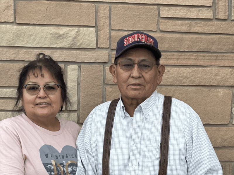 A man wearing a "Semper Fi" cap stands with a woman outside a building, with her grasping his arm.
